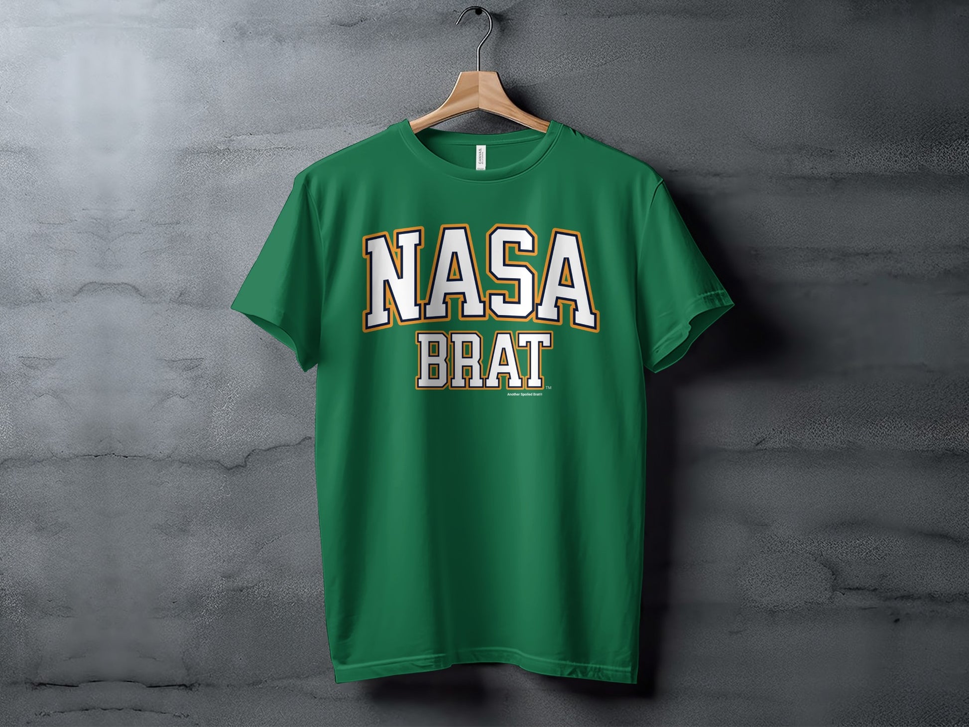 Green t-shirt with white and gold "NASA BRAT" text hanging on a wooden hanger.