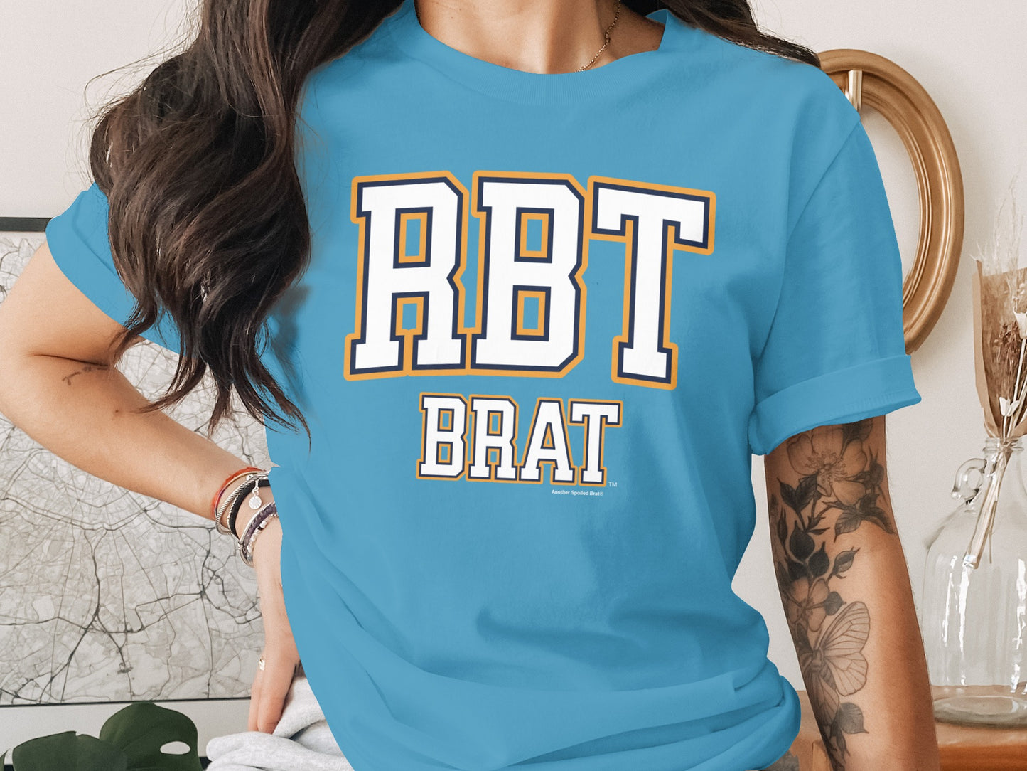 Light blue t-shirt with "RBT BRAT" in white, navy, and orange varsity letters.