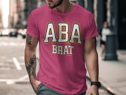 Pink t-shirt with "ABA BRAT" text in white and gold lettering.