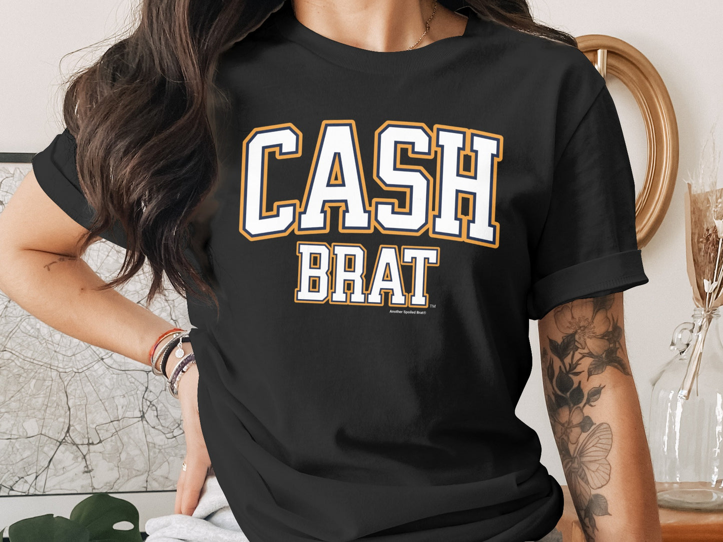 Black t-shirt with white and orange text "CASH BRAT"