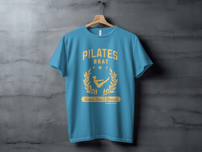 Teal t-shirt with "Pilates Brat" text, laurel wreath, and woman posing.