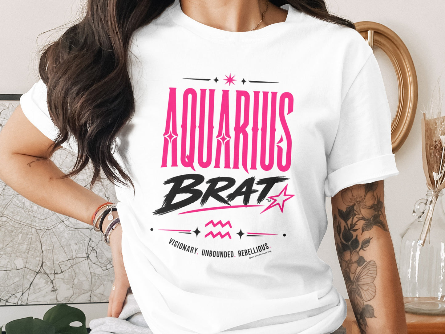 White t-shirt with "AQUARIUS BRAT" and "VISIONARY. UNBOUNDED. REBELLIOUS." text printed in pink and black.