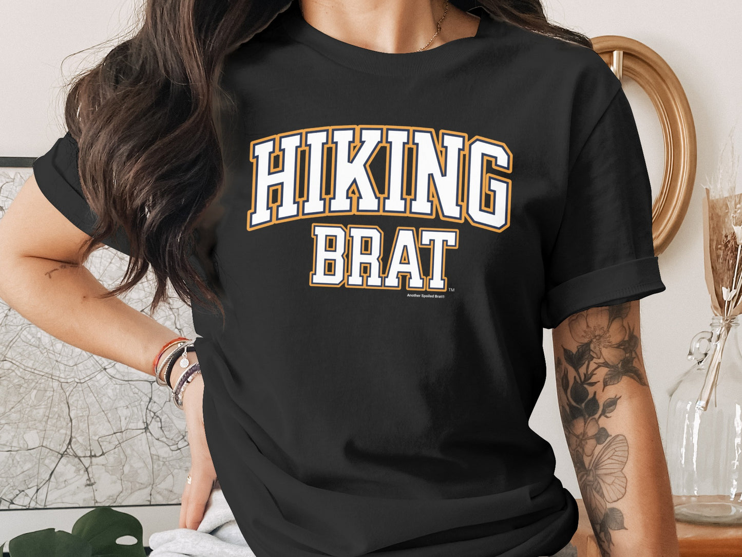 Black t-shirt with "HIKING BRAT" text in white with orange and blue outlines.