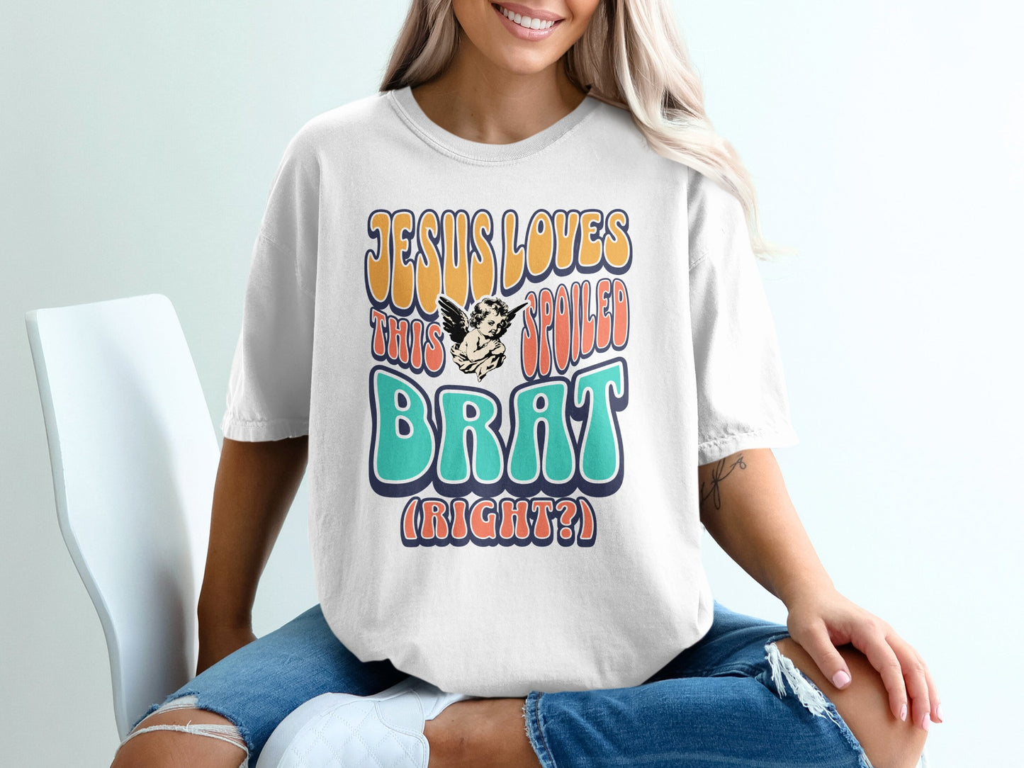 White t-shirt with "Jesus Loves This Spoiled Brat (Right?)" text and cherub graphic.
