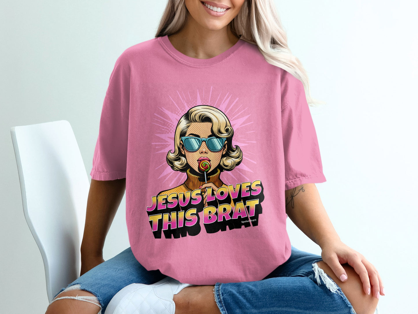 Pink t-shirt with "JESUS LOVES THIS BRAT" text and woman holding lollipop.