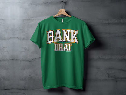 Green t-shirt with white and gold "BANK BRAT" text against a concrete background.