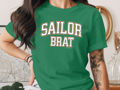 A person wearing a green short-sleeved t-shirt with Sailor Brat printed in white lettering on the chest.