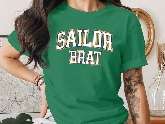 A person wearing a green short-sleeved t-shirt with Sailor Brat printed in white lettering on the chest.