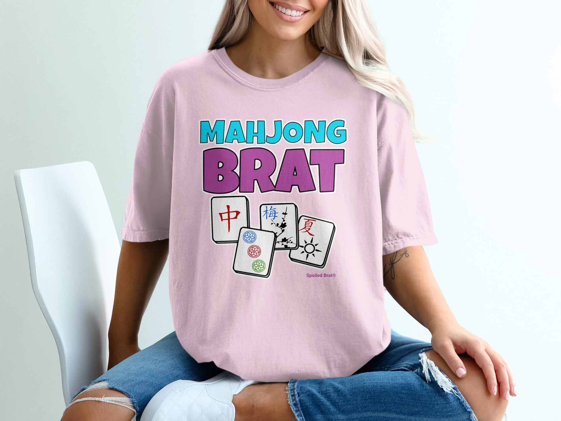 Mahjong Brat text with Mahjong tiles and a woman wearing a pink t-shirt.