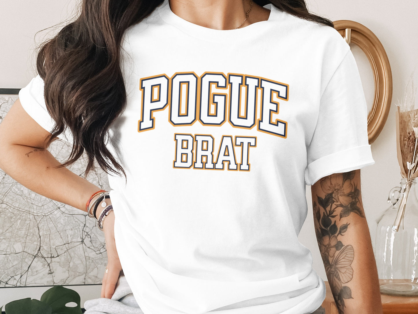 White t-shirt with "POGUE BRAT" text in navy blue and gold collegiate font.