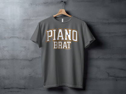 A grey t-shirt hangs on a wooden hanger with "PIANO BRAT" printed in white and orange collegiate font.