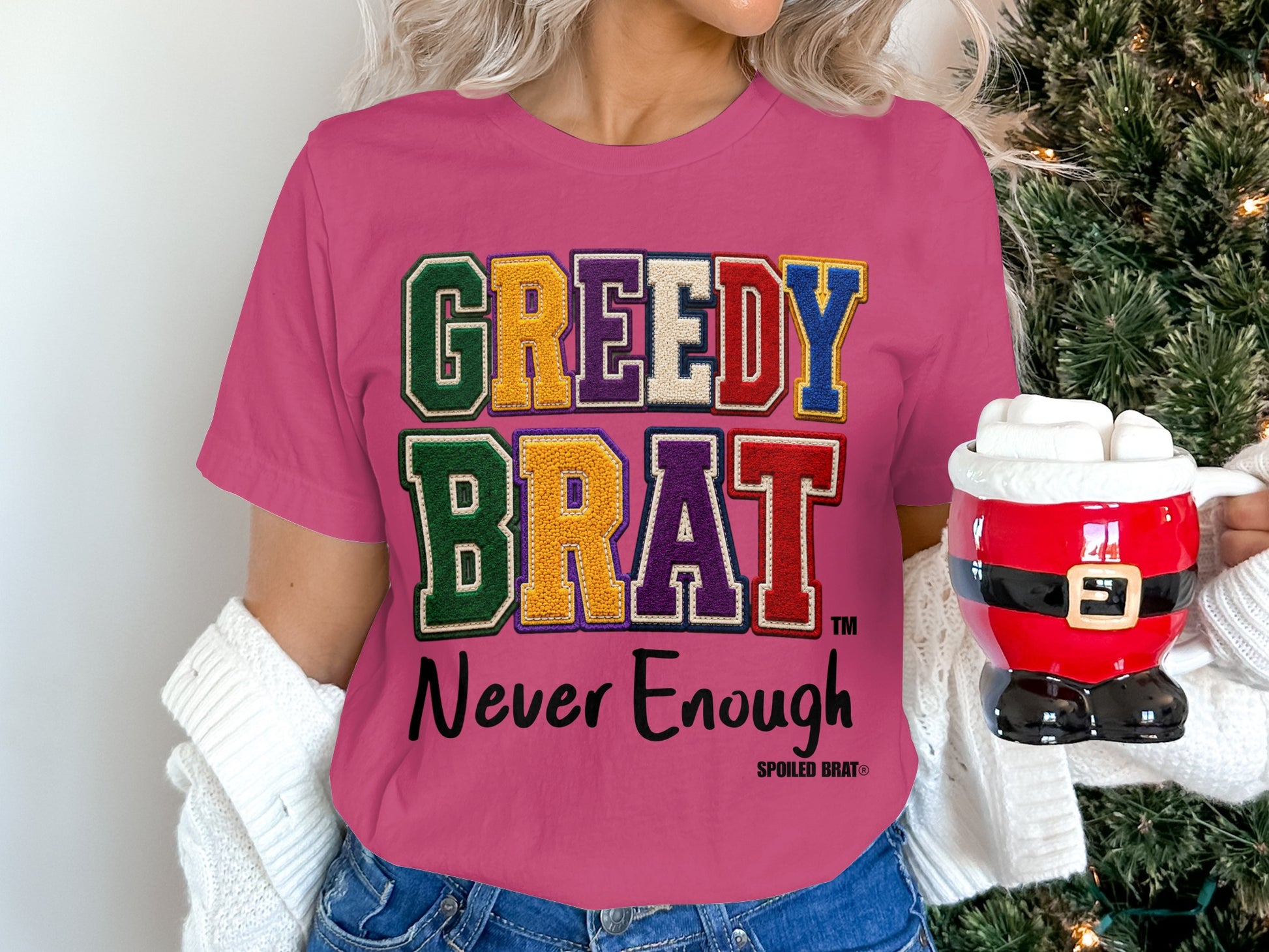 Pink t-shirt with "GREEDY BRAT" and "Never Enough" text, a Santa mug, and a Christmas tree.