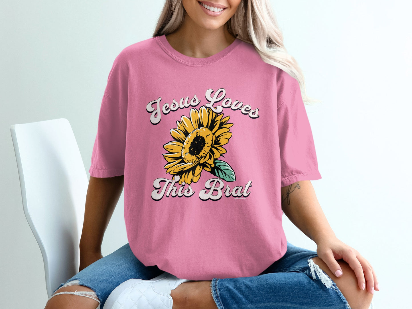 Pink t-shirt with "Jesus Loves This Brat" and a sunflower graphic.