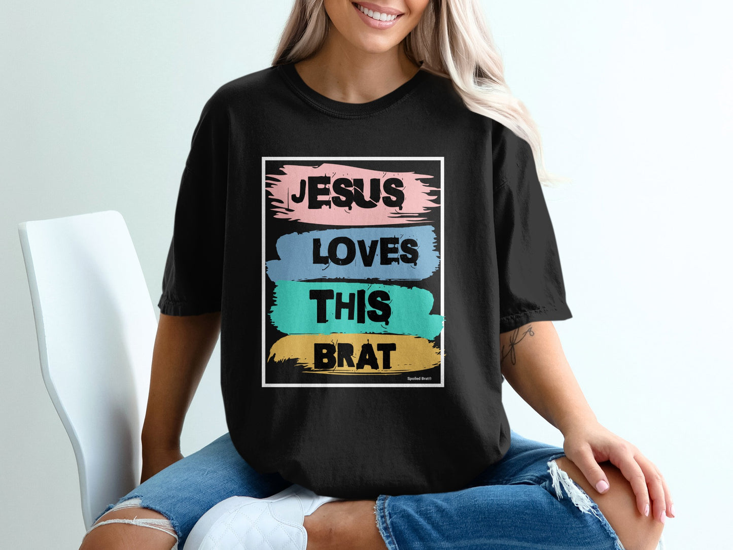 Black t-shirt with "JESUS LOVES THIS BRAT" text in colorful brush strokes.