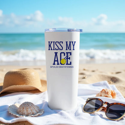 White tumbler with "KISS MY ACE" and tennis ball graphic on a beach.