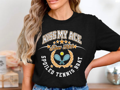 Black t-shirt with "Kiss My Ace Spoiled Tennis Brat" text and tennis graphics.