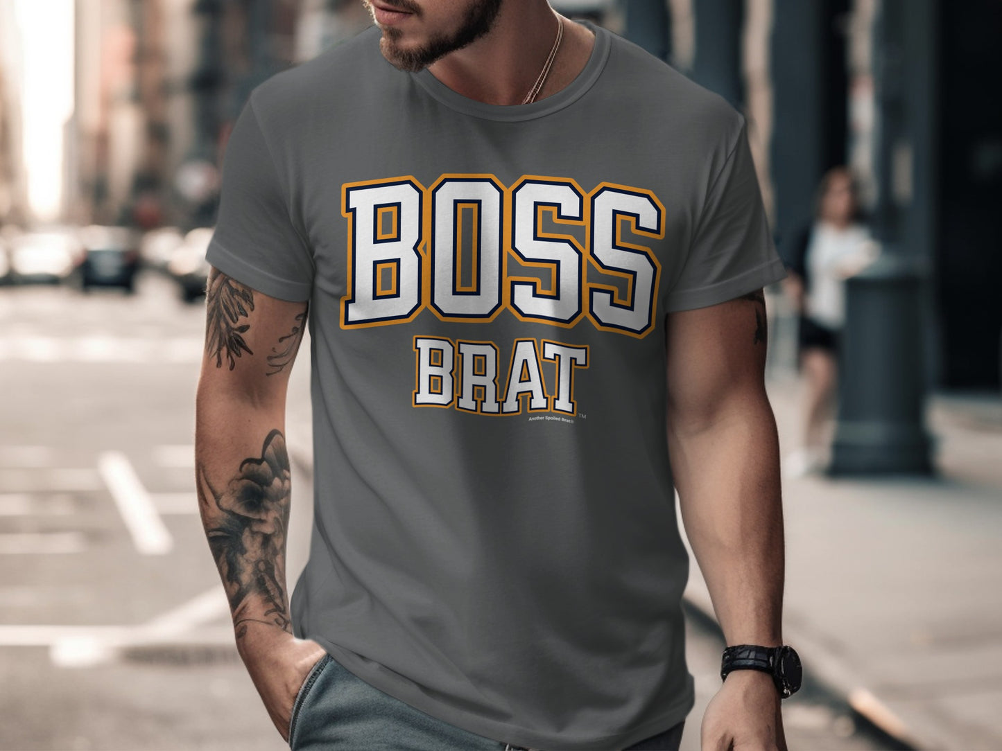 Man wearing gray t-shirt with "BOSS BRAT" text on chest, outdoor city background.