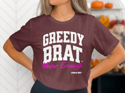 Maroon t-shirt with white "GREEDY BRAT" and pink "Never Enough" text.