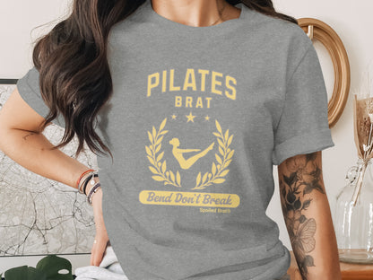 Grey t-shirt with "PILATES BRAT" text, laurel wreath, and "Bend Don't Break" slogan.