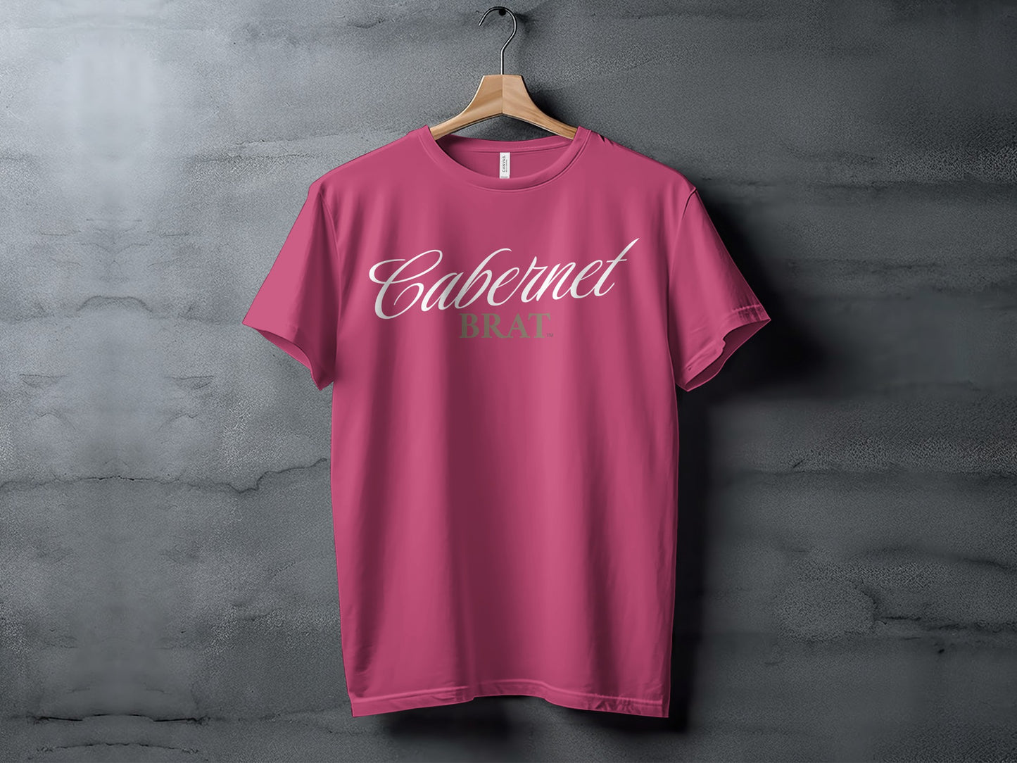 Pink t-shirt with "Cabernet BRAT" graphic, hanging on a wooden hanger.