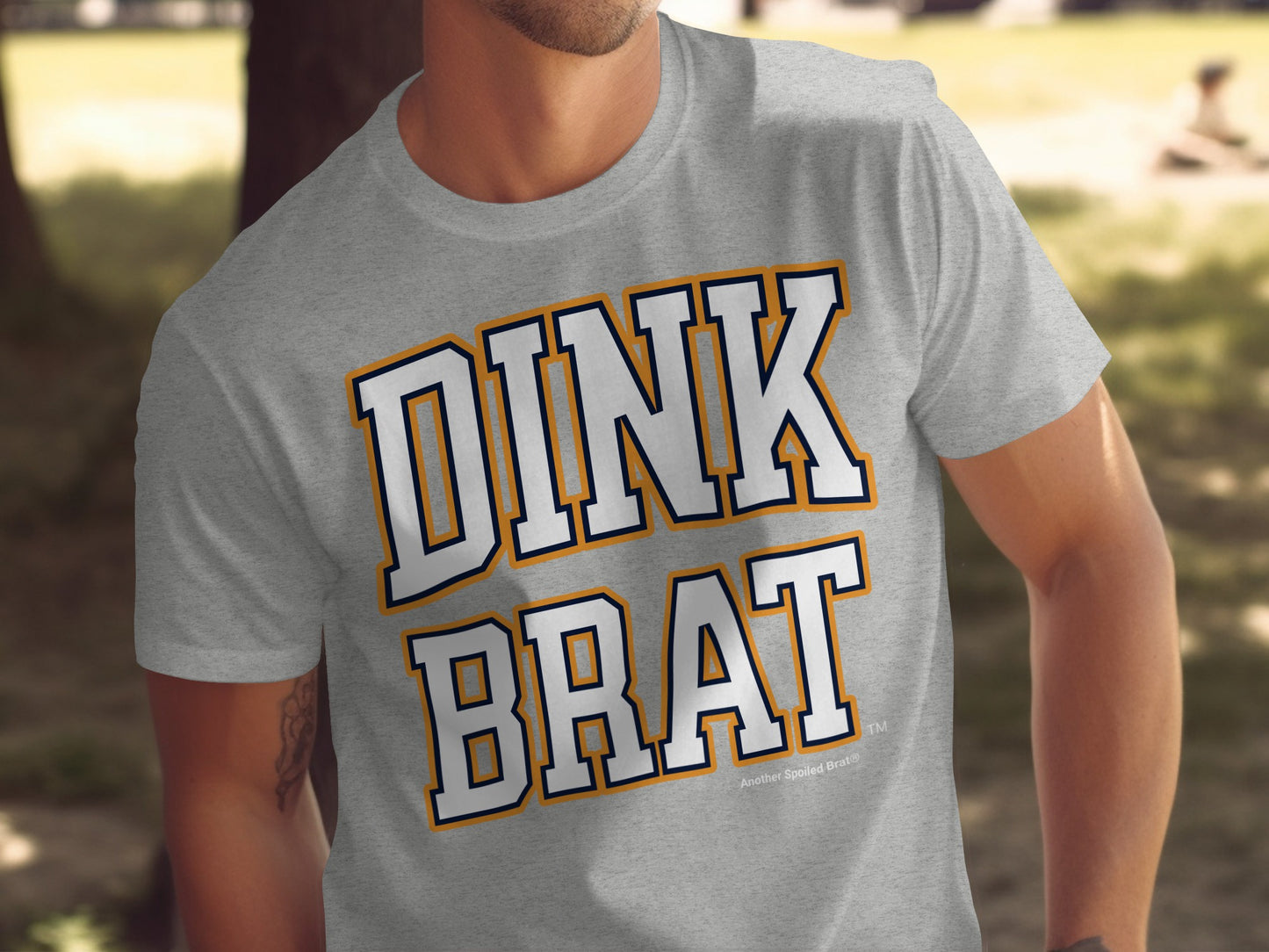 Grey t-shirt with "DINK BRAT" text in layered orange and navy outline.