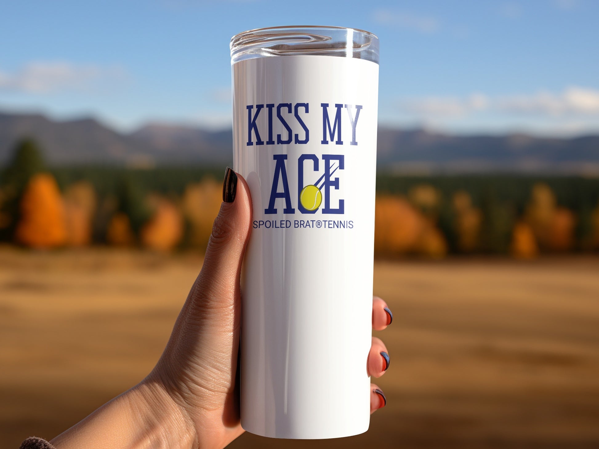 White tumbler with "KISS MY ACE" and a tennis ball, held by a hand.