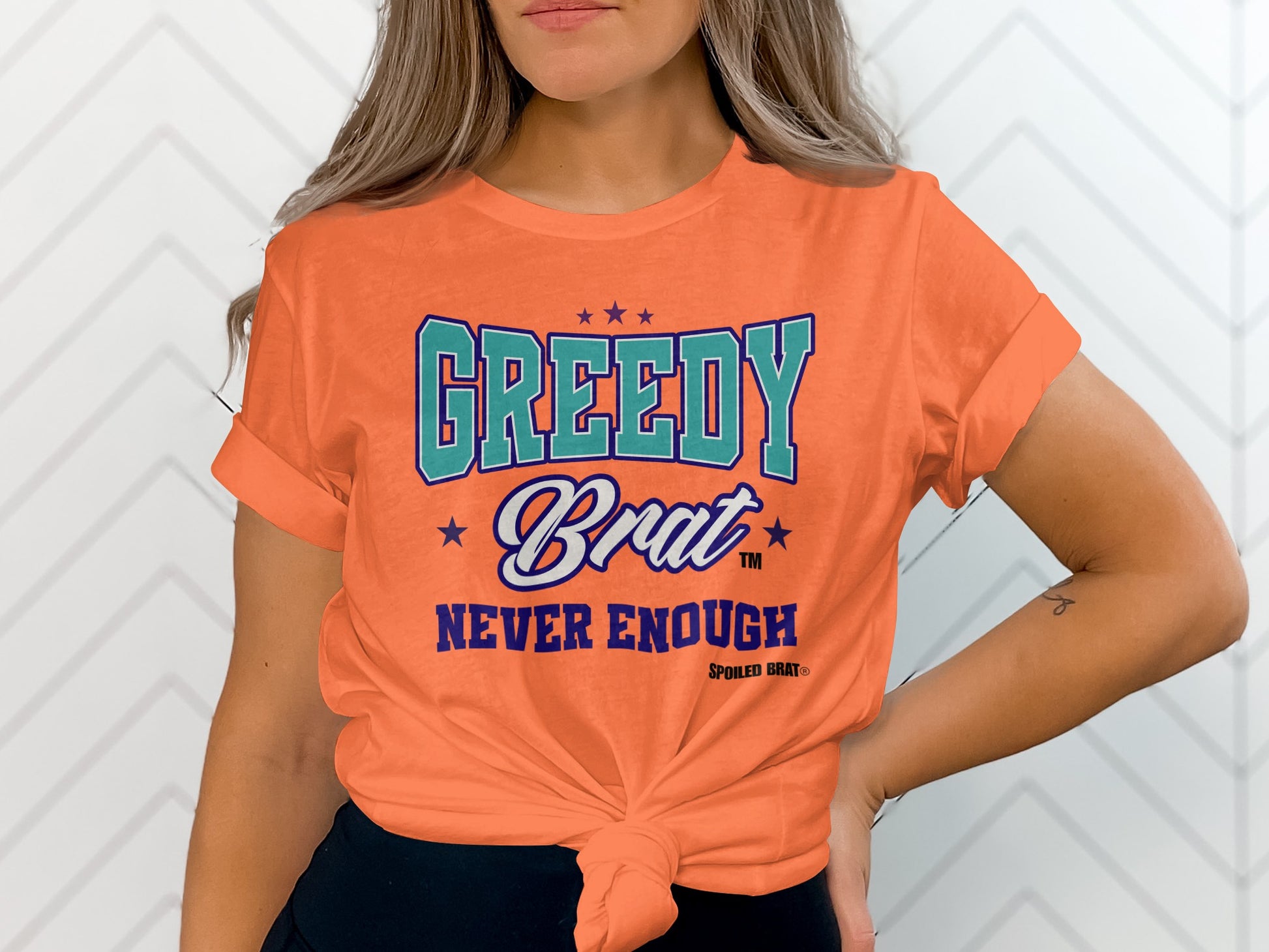 Orange t-shirt with "GREEDY Brat NEVER ENOUGH" text and stars.
