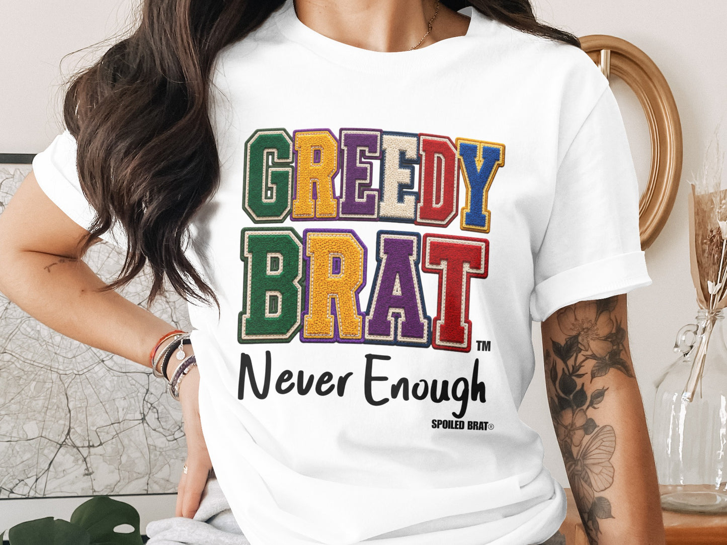 White t-shirt with "GREEDY BRAT" text and "Never Enough" slogan.