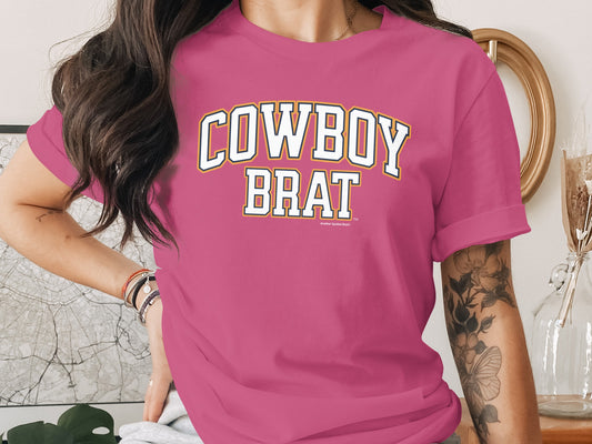 Pink t-shirt with "Cowboy Brat" text in white and yellow collegiate lettering.