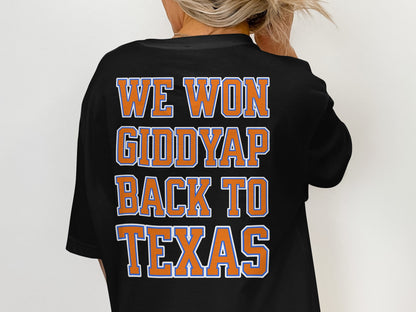 Black t-shirt with orange and blue text reading "WE WON GIDDYUP BACK TO TEXAS".