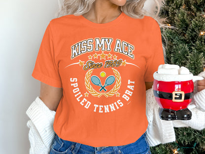 Orange t-shirt with "Kiss My Ace Spoiled Tennis Brat" and crossed racquets.