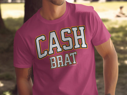 Pink t-shirt with white and gold "CASH BRAT" text in collegiate lettering.