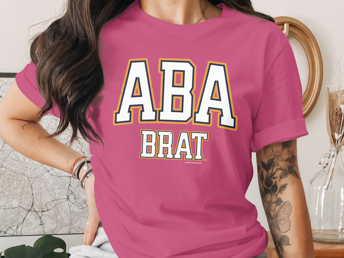 Pink t-shirt with "ABA BRAT" and "Another Spoiled Brat" text and embroidered trim.