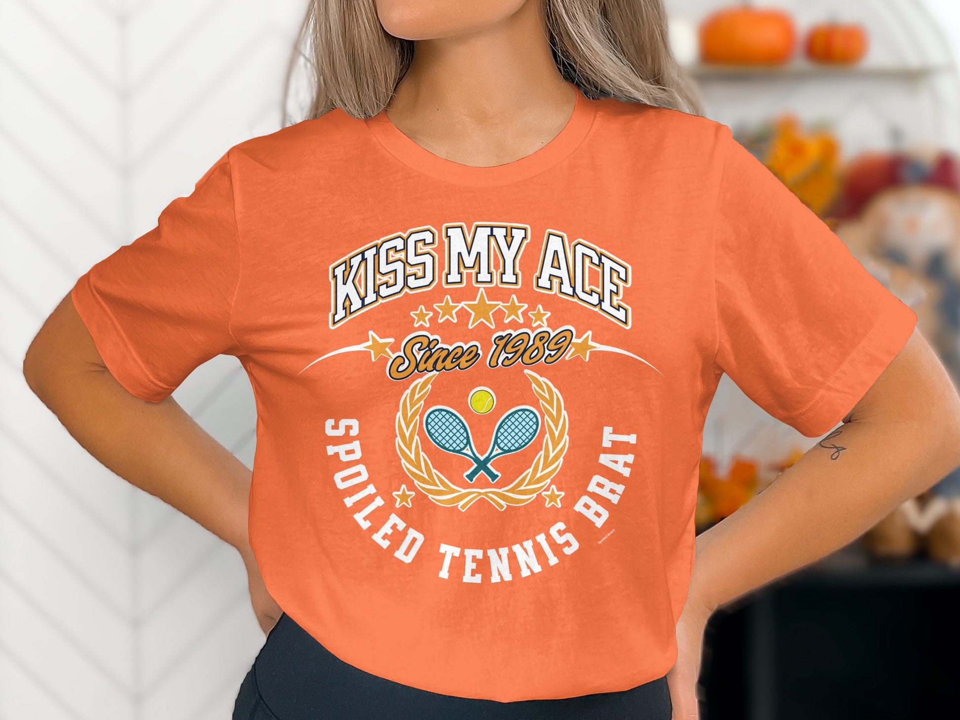 Orange t-shirt with "Kiss My Ace Spoiled Tennis Brat" and tennis racket/ball graphic.