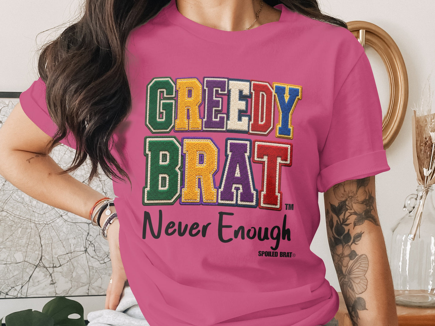 Pink t-shirt with "GREEDY BRAT Never Enough" text graphic.