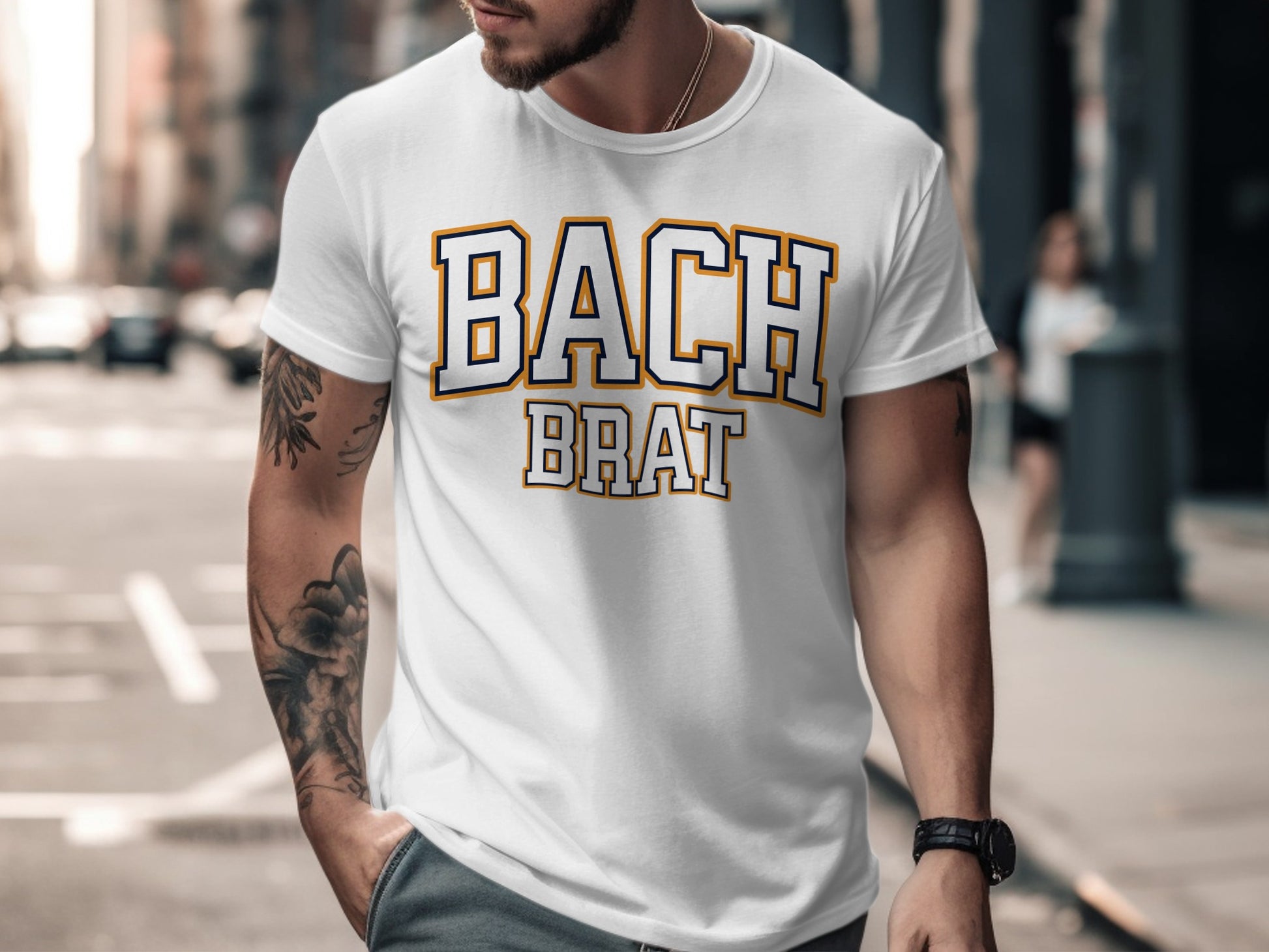 White t-shirt with "BACH BRAT" text in collegiate font with navy and gold outline.