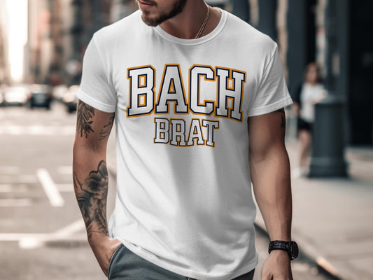 White t-shirt with "BACH BRAT" text in collegiate font with navy and gold outline.