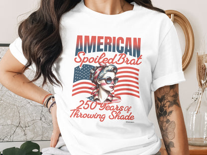 Woman wearing a t-shirt with "AMERICAN Spoiled Brat 250 Years of Throwing Shade" and a patriotic design.