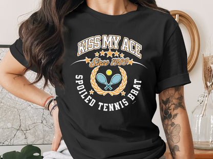 Black t-shirt with "Kiss My Ace Spoiled Tennis Brat" text and tennis graphics.