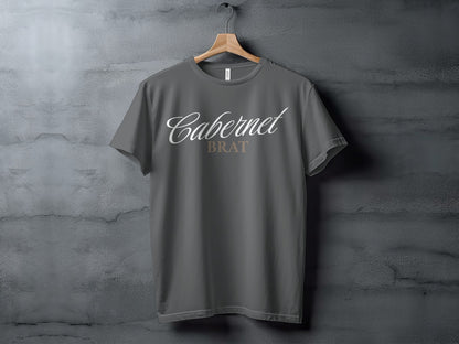 Dark grey t-shirt featuring "Cabernet BRAT" text in white and beige on a wooden hanger.