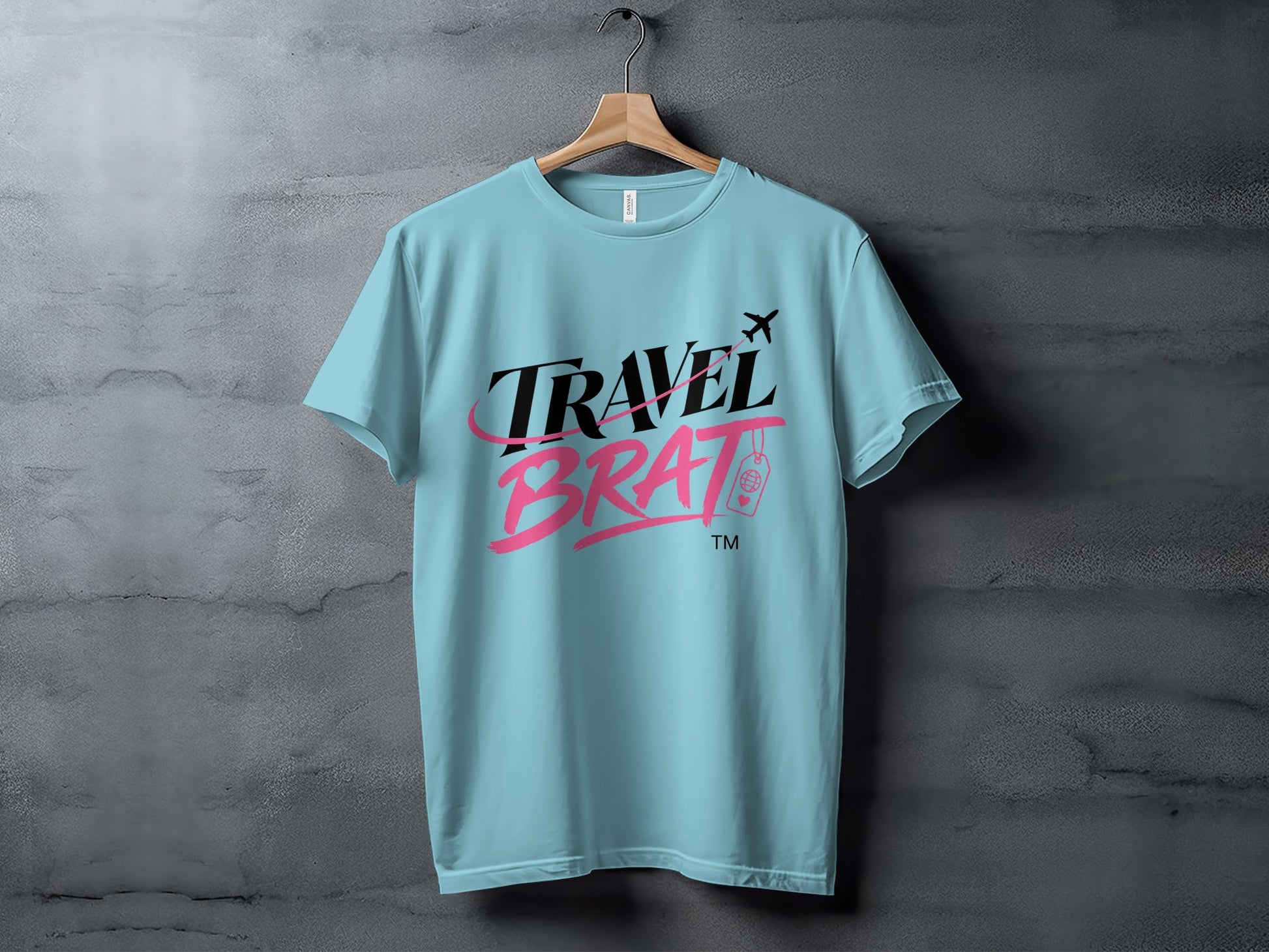 Light blue t-shirt with "TRAVEL BRAT" text, airplane, and luggage tag graphic.