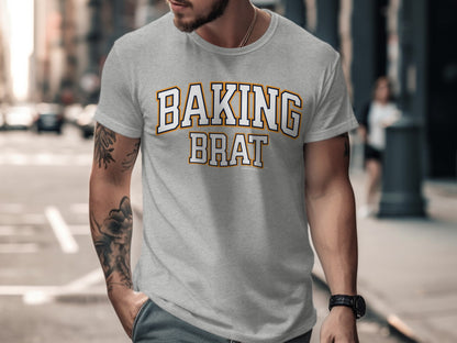 Light grey t-shirt with "BAKING BRAT" in collegiate font, standing on a city street.