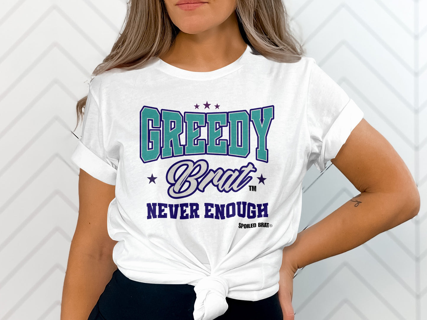 White t-shirt with "GREEDY Brat NEVER ENOUGH" graphic and trademark symbols.
