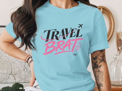 Light blue t-shirt with "TRAVEL BRAT" text, airplane, and globe icon.