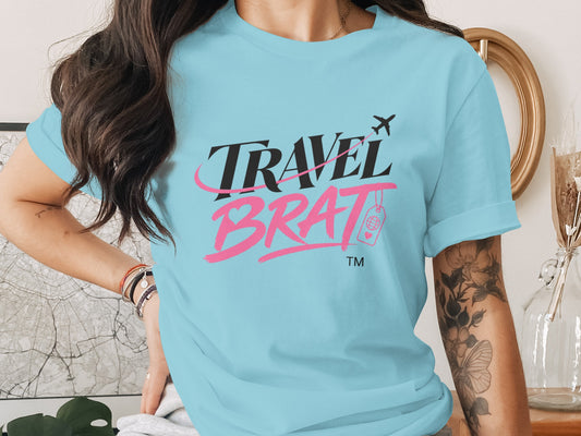Light blue t-shirt with "TRAVEL BRAT" text, airplane, and globe icon.