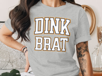 Grey t-shirt with white and orange "DINK BRAT" text and "Another Spoiled Brat" logo.