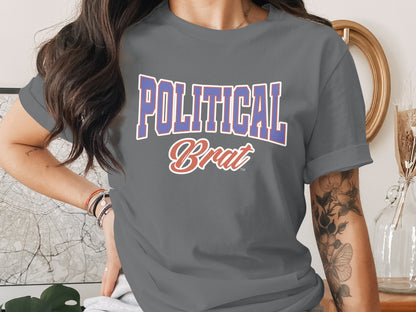 Graphic t-shirt with "POLITICAL Brat" text, worn by a person with tattoos and jewelry.