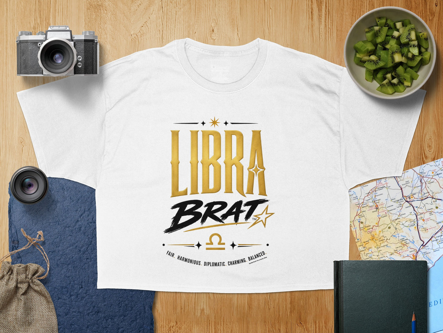 White t-shirt with "LIBRA BRAT" text, Libra symbol, and descriptive words.