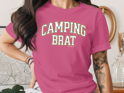 Pink t-shirt with white and yellow "CAMPING BRAT" graphic text.
