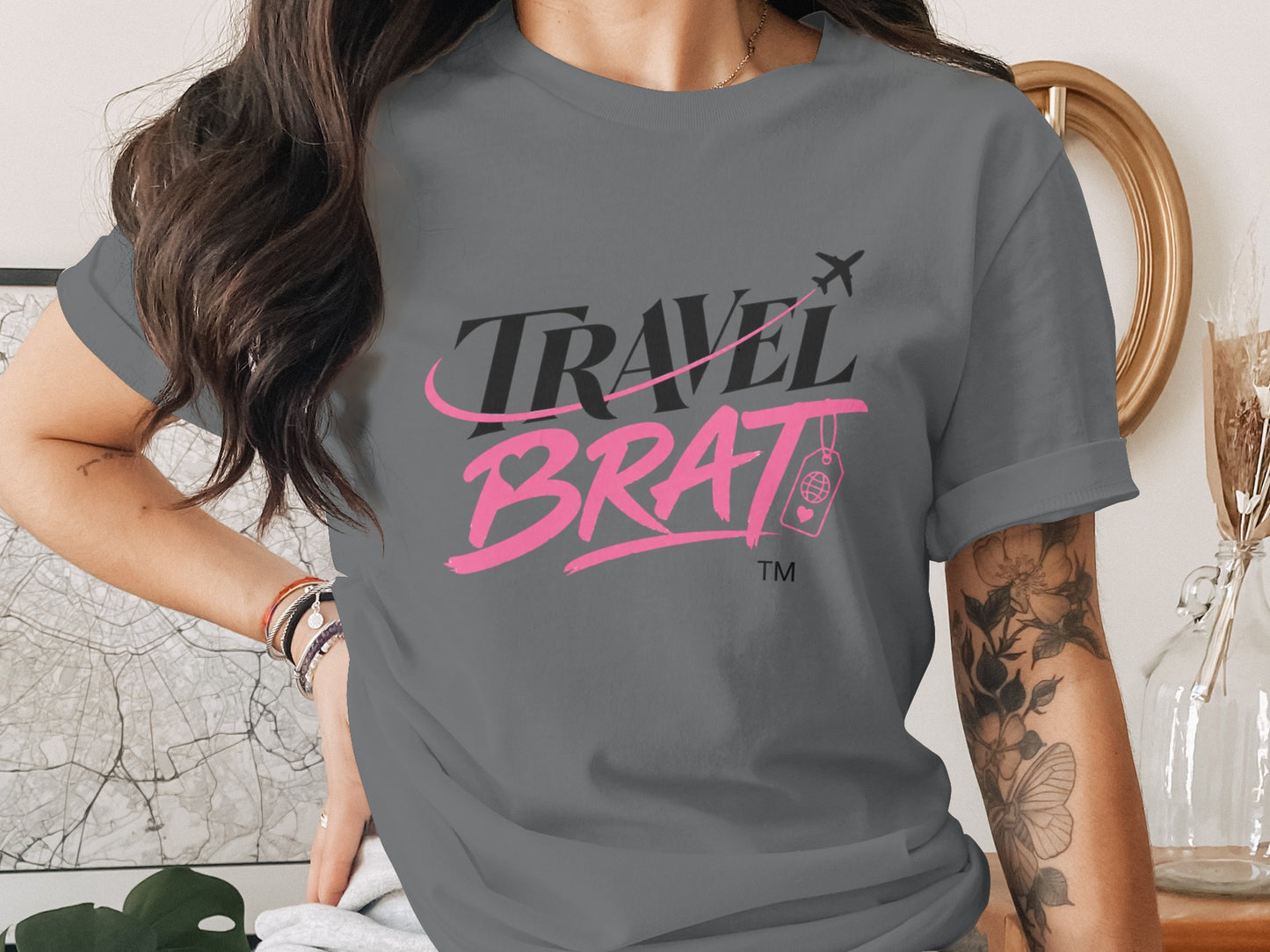 Gray t-shirt with black and pink "TRAVEL BRAT" text and airplane graphic.